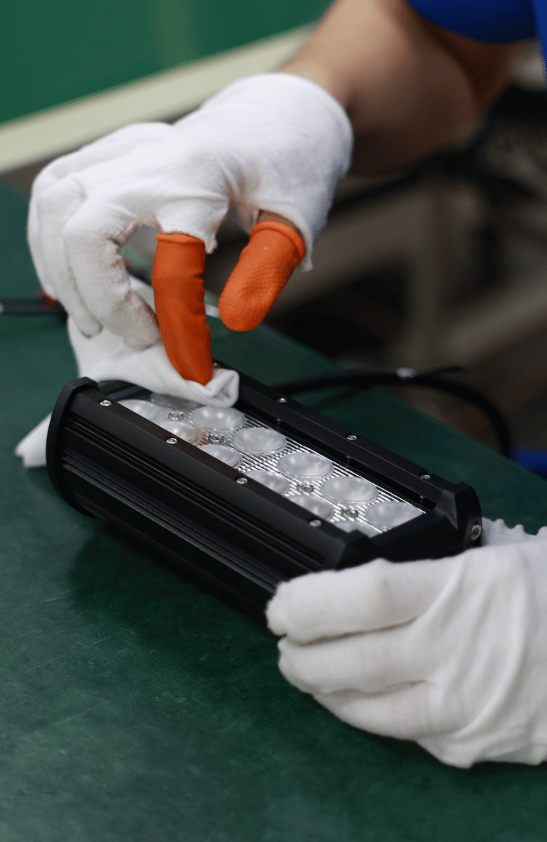 Gloved hands cleaning and inspecting the lens of an LED light bar during final QC