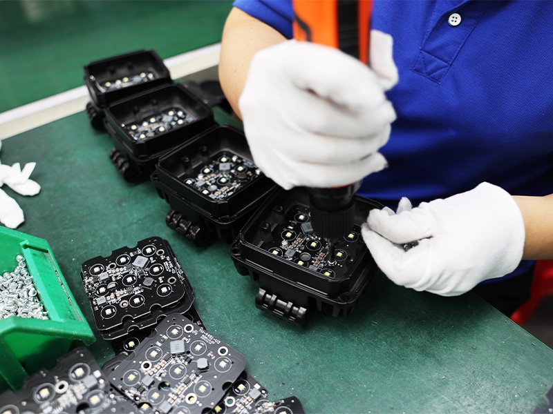 A technician fastening an LED circuit board into a work light housing during assembly